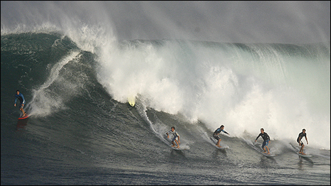 Six surfers ride a wave in Waimea, Hawaii. 