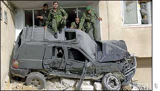 Palestinians clamber over a car crushed against a doorway by Israeli armour
