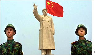 Two Chinese soldiers stand in front of a statue of Mao