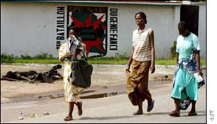 Bouake residents fleeing the fighting walk past the corpse of a government soldier  