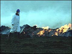 Farmer dressed in protective clothing surveying burning pyre  