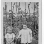 Peter with cousin Anne in July 1944.  Italian Prisoner of War Camp in background behind the runner beans. Ash near Aldershot.