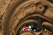 Abstract plant carvings around the top of a stained-glass window, which could be maize or corn