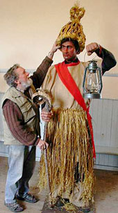 Renowned model maker Gordon Johnson removes the conical shaped straw pleated hat from Captain Mummer, who is holding a goat horned staff and hurricane lamp
