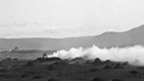 A figure tends to a smoking fire in a field covered with small heaps of seaweed.