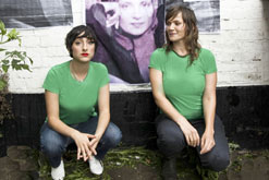 Comedians Miriam Elia and Jessica Stevenson in front of a poster of Hengemeh