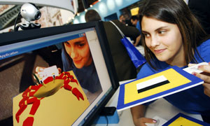 Girl using Augmented Reality service. Girl is holding a paddle. She is looking at a computer screen which shows a picture of herself holding the paddle with a digitised crab on it