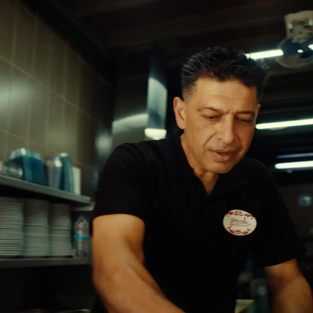 Chef in black polo shirt preparing food in a professional kitchen setting.