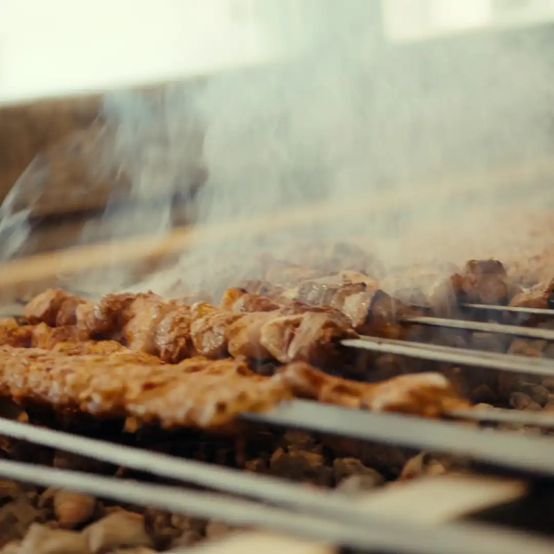 Skewers of marinated meat grilling over hot charcoal with rising smoke.