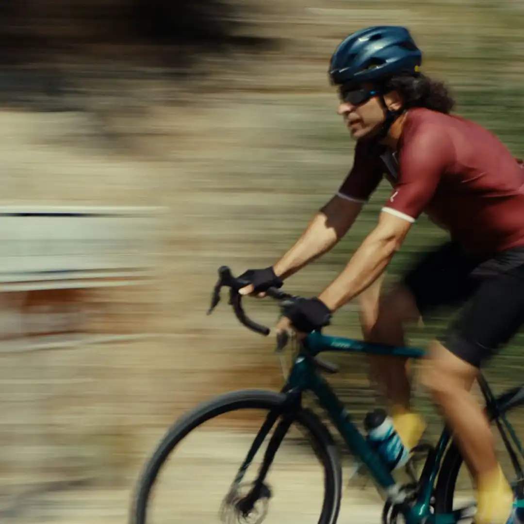 A solo cyclist pedals uphill on a curving mountain road, surrounded by nature and rocky terrain.