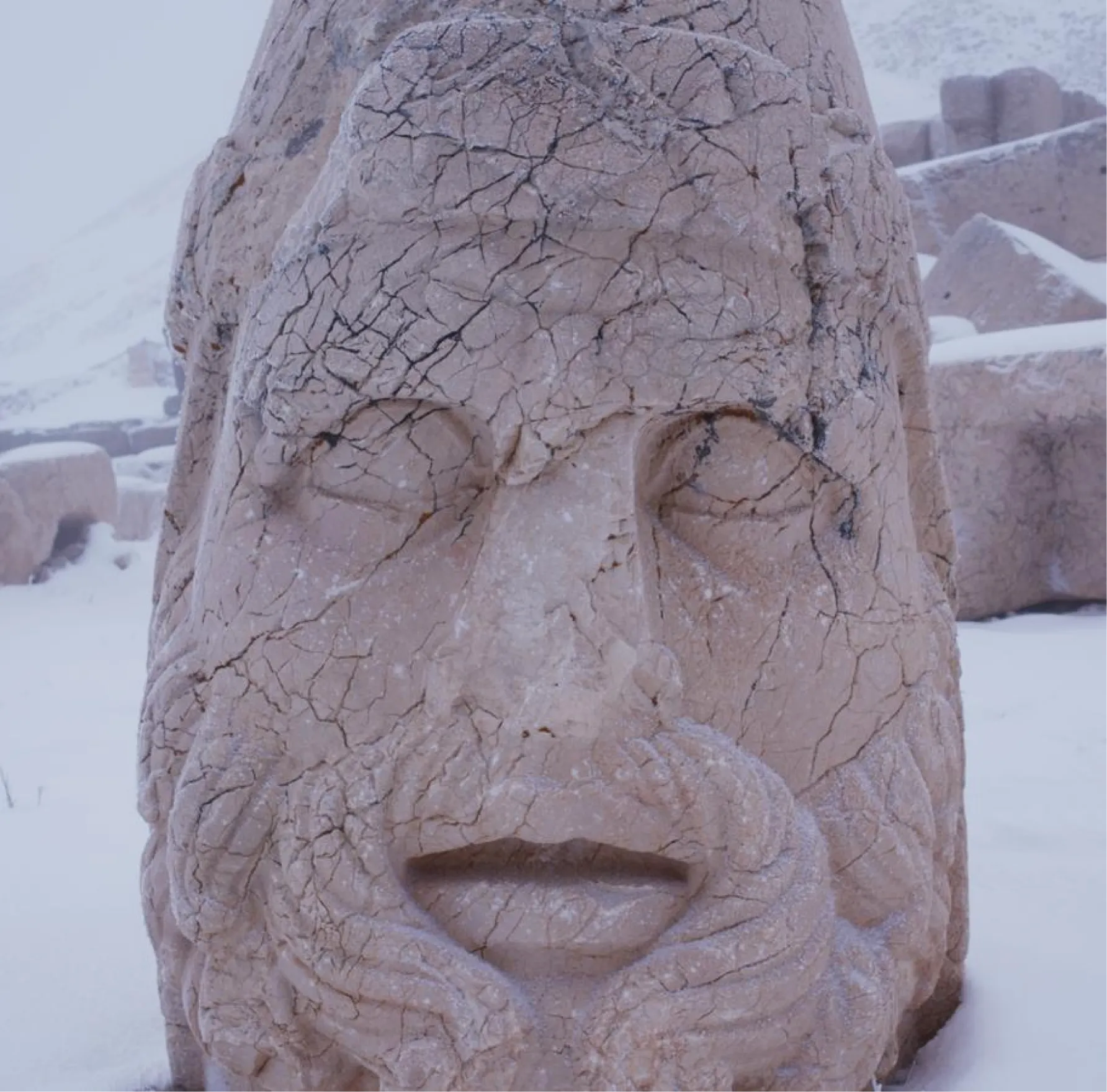 Ancient stone head sculpture with a beard and crown, frosted over with snow on Mount Nemrut.