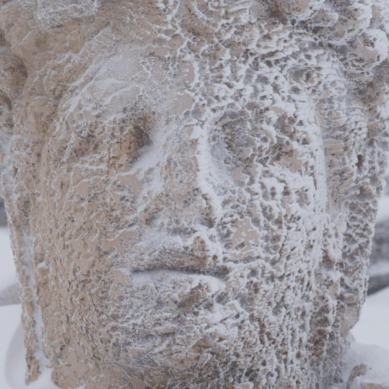 Close-up of a cracked, weathered stone head statue with beard, dusted lightly in snow at Mount Nemrut.
