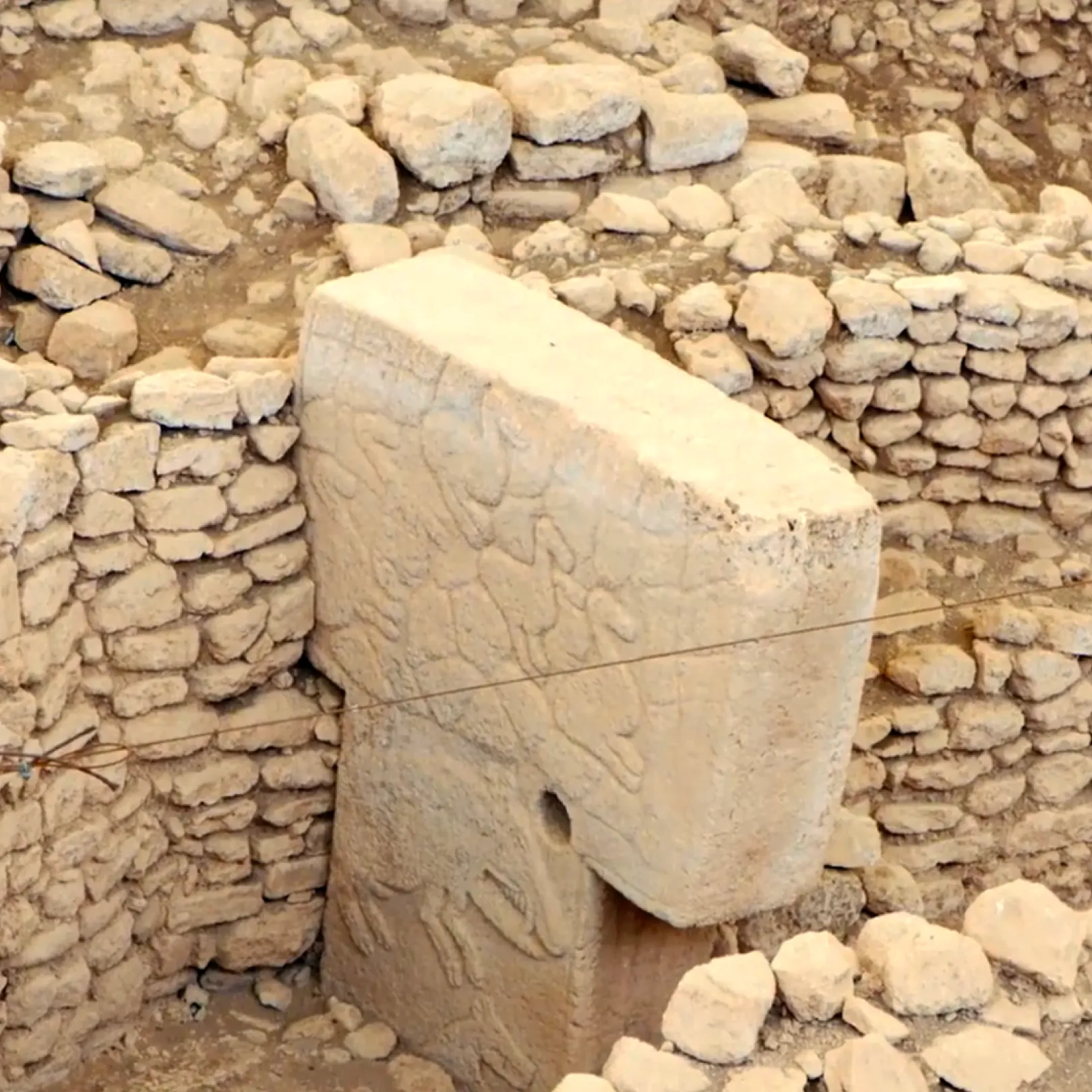 Detail of an ornately carved T-shaped stone pillar at Göbekli Tepe, surrounded by low stone walls from the Neolithic structure.